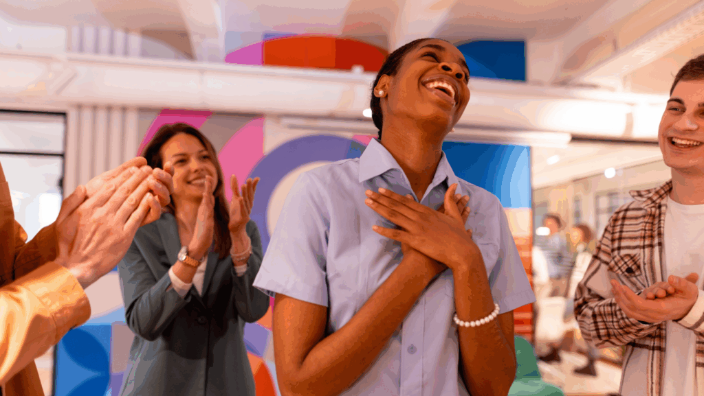 Group of people standing indoors, clapping and showing appreciation in a brightly lit modern space with colorful geometric wall art in the background.